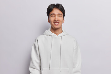 Portrait of handsome Asian man with dark hair dressed in casual sweatshirt smiles pleasantly looks...