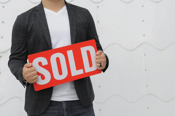 man in a business casual attire clothes holding up a sold sign