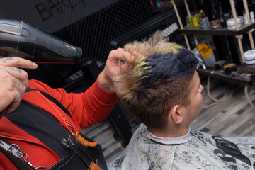 Close-up of a man's hands of a professional barber blow drying hair to a client guy in a...