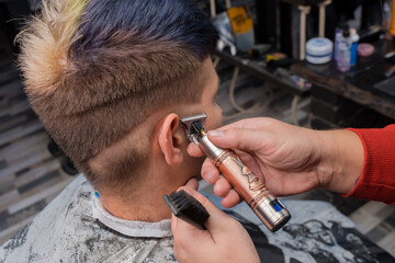 The hands of a male hairdresser in the salon shave the temporal region, cut a young guy of a client...