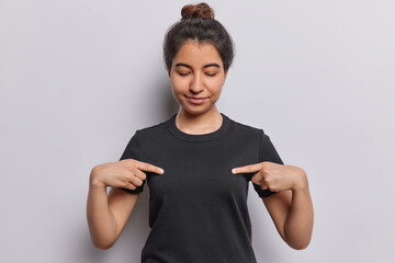 Horizontal shot of pretty girl with dark hair showcases her new black casual tshirt against studio...