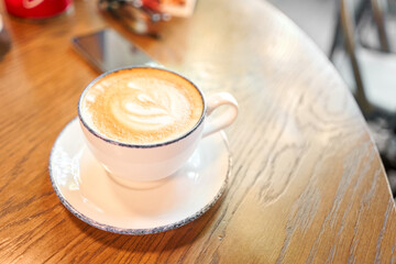 A cup of hot cappuccino on the table in the coworking space of the coffee shop. A cup of coffee on the veranda on a sunny day. Coffee break at the cafe. Close-up