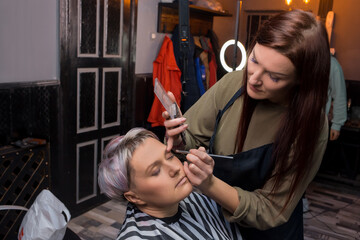 Girl hairdresser makes a make-up with a palette of shadows to an adult cute woman to a client of a barbershop salon services hairstyle, coloring