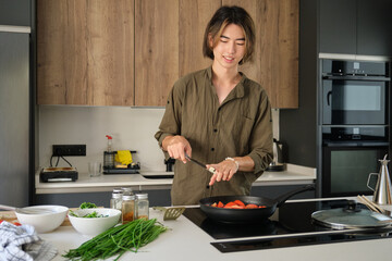 Smiling asian young man cooking chinese or taiwanese tomato scrambled eggs at kitchen.