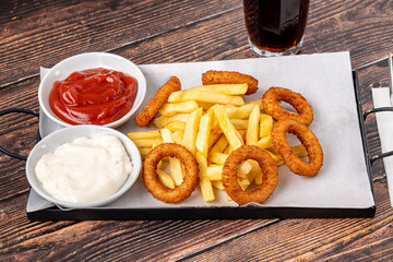 Onion rings and french fries with ketchup and mayonnaise on wooden table