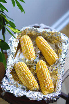 Raw corn on cobs in a baking dish. Prepare corn before cooking. Vegetable season. Fresh corn cobs prepared for cooking baked corn. Healthy eating. Vegan food concept, vertical image