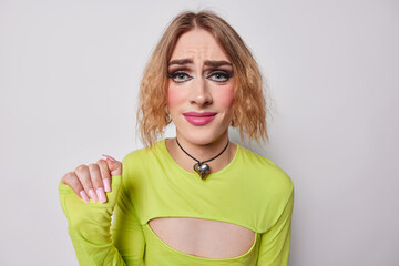 Horizontal shot of displeased transgender woman with bob hairstyle keeps hand raised up has long nails dressed in green fashionable jumper wears bright makeupp isolated over white background