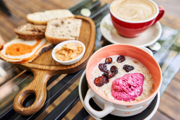 Breakfast with fresh cooked porridge served with Dry Cherry with strawberry sorbet in bowl. Assorted sliced bread on a wooden board. Served with smoked butter. Breakfast with cappuccino coffee.
