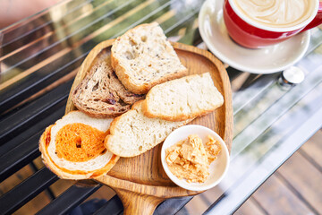Assorted sliced bread on a wooden board. Served with smoked butter. Breakfast with cappuccino coffee. Composition with butter and bread on wooden plate.