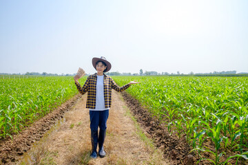 Wide angle of Asian farmer woman wear shirt standing and holding Thai banknote at green corn farm
