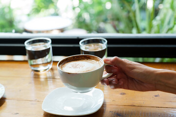 Close-up of Asian woman's hands He is using his right hand to hold a cup of latte coffee. with full glass lift up ready to eat In the coffee shop. women drinking coffee in the afternoon