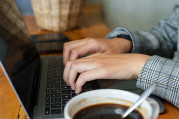 Portrait of hands of young asian businesswoman Typing on a laptop and a cup of coffee next to it for a refreshing drink in a café. On days when you have to work outside