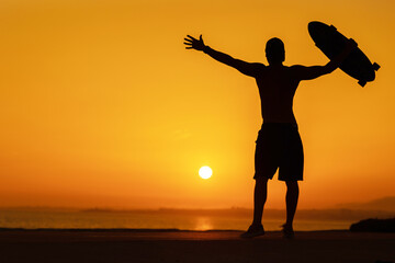 Fototapeta premium Silhouette of a free man holding a skateboard at bright sunset