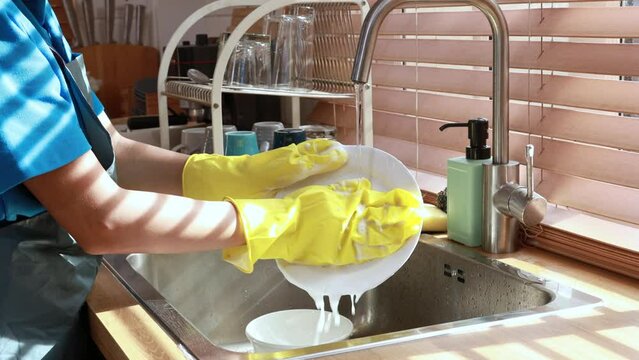 Young professional Asian teenage housewife washing crockery and cleaning the house.