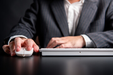 Close up of businessman hand using mouse and typing on computer keyboard sitting working on office workplace desk or work from home with copy space background. Business people and technologt concept.