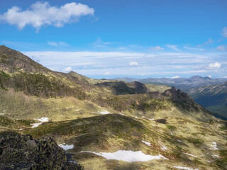 Bright sunny atmospheric scenery on top of spotted mountain ridge under white clouds and blue sky. Beautiful landscape above mountain range with sunlight. Western Sayans.