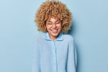 Happy overjoyed curly haired young woman laughs joyfully dressed in casual jumper expresses...