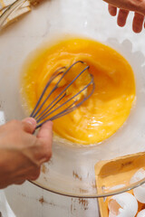 top view of woman beating eggs for an omelette or pie. Cook delicious and healthy food at home for breakfast. A whisk or mixer for convenience of cooking protein dish. broken eggshells and paper box