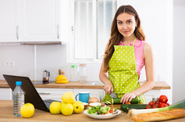 Obraz na płótnie Canvas Young housewife using laptop and cooking in home kitchen