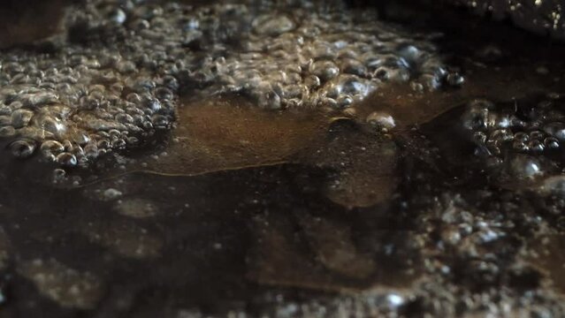 A close-up macro video of a bubbling dark oily liquid. Viscous crude oil bubbles and boils from a natural geothermal source. The thick glossy black oil gurgles as steam escapes violently from the heat