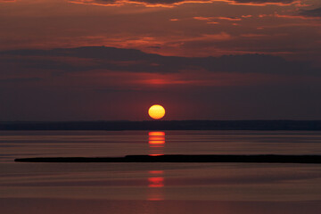 Sunset over the river on a summer evening. The sun is coming down to the horizon. The sky and water...
