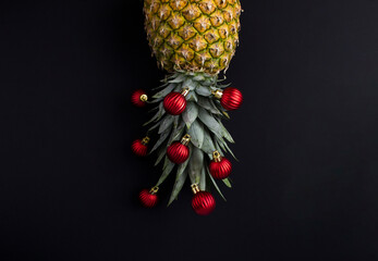 Pineapple with red Christmas bead on the black background. Copy space. Christmas composition.
