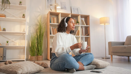 Enjoying coffee. Domestic comfort. Cozy leisure. Serene dreamy woman drinking beverage listening music in headphones home living room on floor.