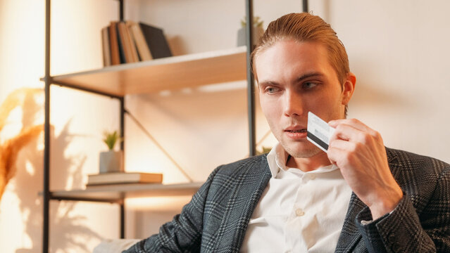 Confusing banking. Transaction risk. Bank loan. Pensive perplexed puzzled anxious business man with credit card thinking at modern home interior with free space.