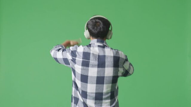 Back View Of Young Asian Teen Boy Holding A Microphone And Rapping On The The Green Screen Background
