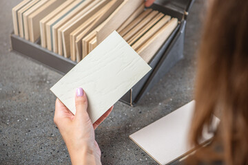 A woman interior designer chooses a color sample from chipboard. The choice of wood material for the interior project from chipboard or natural wood samples. Design or architecture concept. - obrazy, fototapety, plakaty