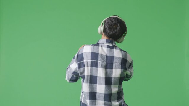 Back View Of Young Asian Teen Boy Wearing Headphone And Holding A Microphone And Singing On The The Green Screen Background
