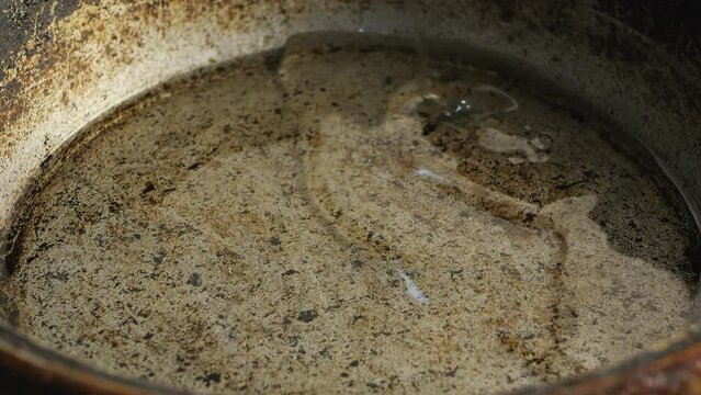 Vegetable oil is poured into a cast-iron skillet heated over a fire. close-up
