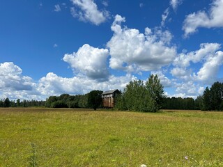 Obraz premium summer landscape, old metal grain dryer, traditional meadow flowers, meadow in summer and wonderful clouds