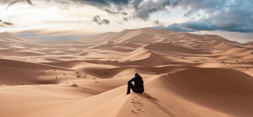 A person sitting in the Erg Chebbi desert in the African Sahara © imagoDens