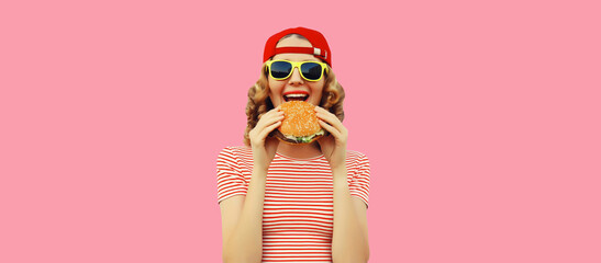 Portrait of stylish smiling young woman with burger fast food on pink background