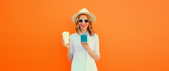 Happy smiling young woman 20s with smartphone and cup of coffee wearing summer straw hat on orange...