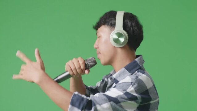 Close Up Side View Of Young Asian Teen Boy Holding A Microphone And Rapping On The The Green Screen Background
