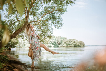 Young 30 year old woman in maxi dress with long legs splashes water on the sea beach. Beautiful...