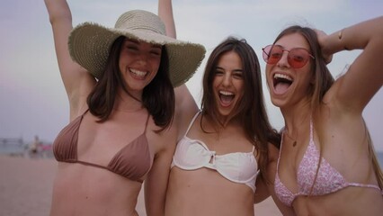 Three excited young Caucasian friends in summer clothes on Mediterranean beach. Group of smiling women enjoying vacation. Cheerful beautiful girls of generation z pose for photo with mobile phone.