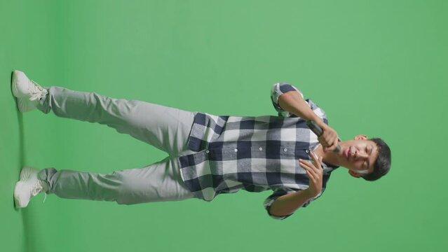 Full Body Of Young Asian Teen Boy Holding A Microphone And Rapping On The The Green Screen Background
