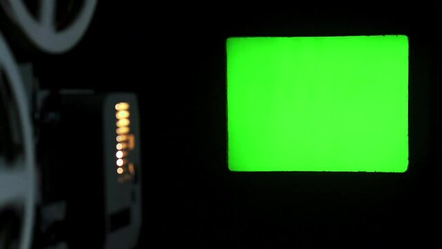 Movie projector displays a green screen on the wall. The film strip turns and the whole environment was in darkness.