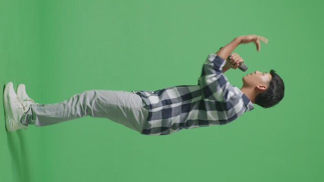 Full Body Side View Of Young Asian Teen Boy Holding A Microphone And Rapping On The The Green Screen Background
