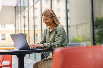 Smiling woman sales manager working on laptop in cafe terrace. Distance work concept