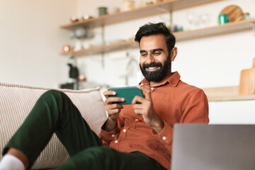 Indian man chilling at home with phone sitting on couch