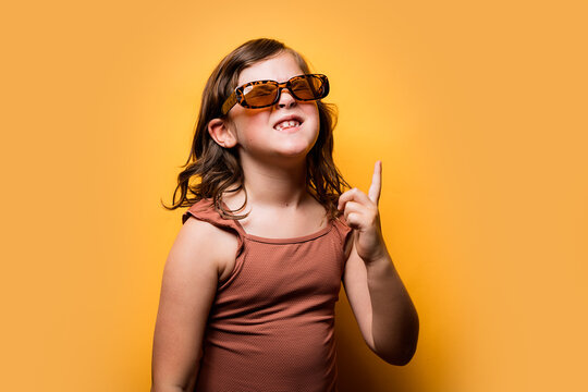 Delighted little kid in summer outfit pointing up in orange studio