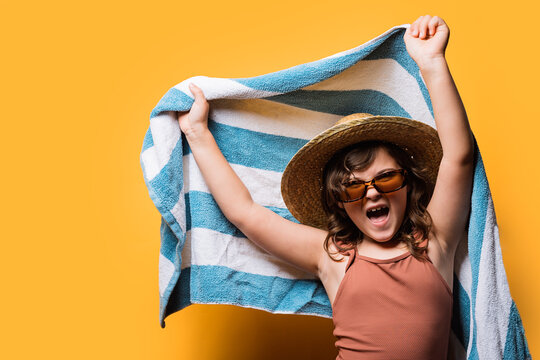 Excited Cute Kid With Towel In Hands Shouting Expressively In Yellow Studio