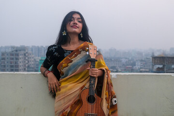 South asian young teenage girl wearing traditional clothings holding a ukulele