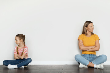 Portrait Of Offended Young Mother And Her Little Daughter Sitting On Floor