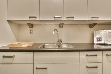 a kitchen with white cupboards and black counter tops on the wall above the sink is a microwave in the corner