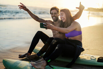 A goofy surfers taking selfies on a beach. - obrazy, fototapety, plakaty